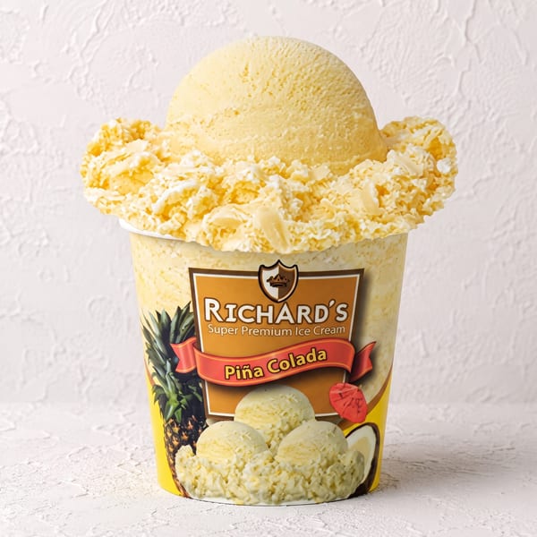 A large scoop of Richard's Piña Colada ice cream with coconut flakes in a branded cup.