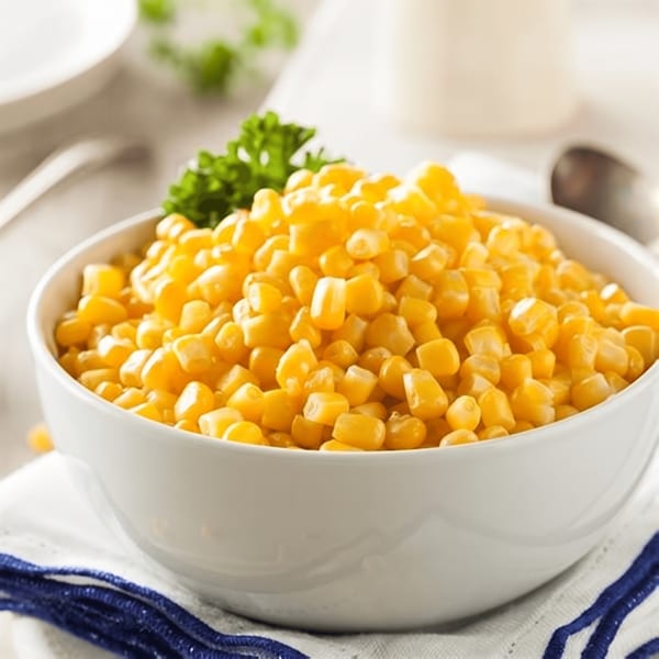 A white bowl filled with bright yellow corn kernels, garnished with a sprig of parsley.